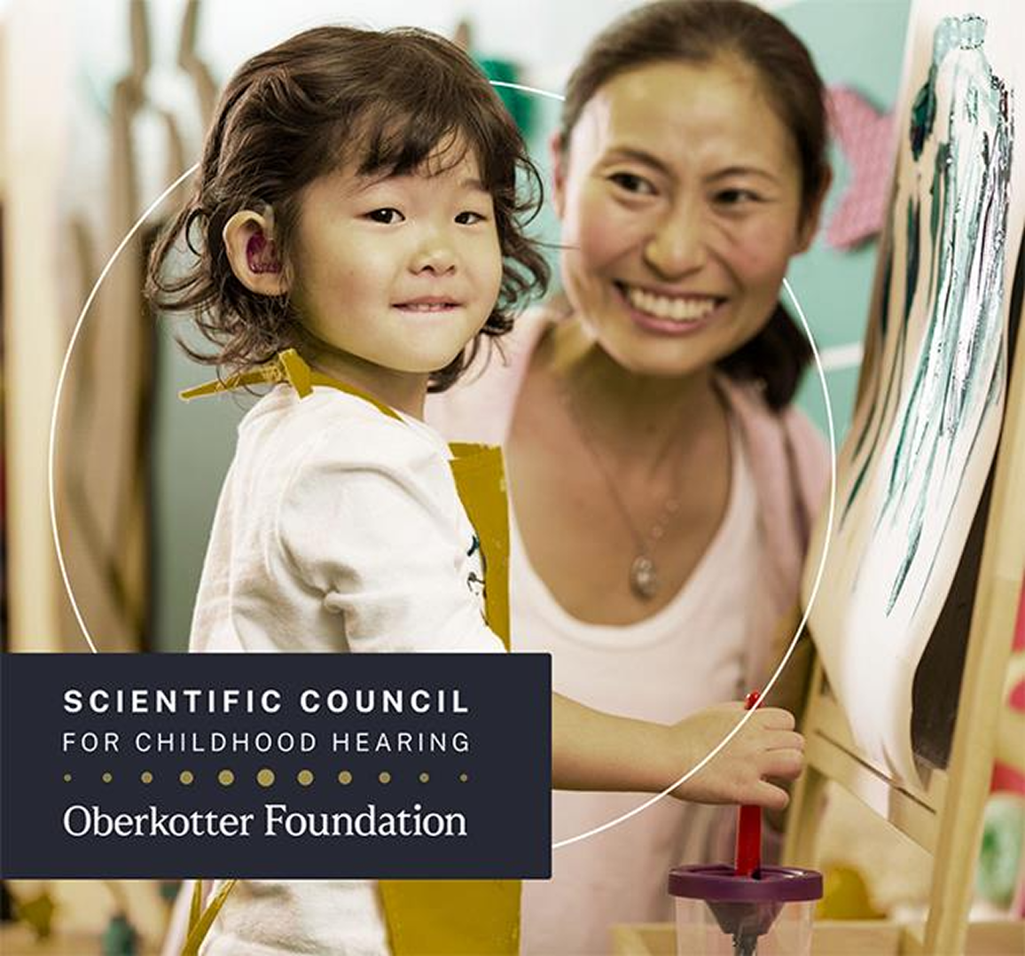 A young girl wearing a hearing device smiles as she stands at an easel, painting. The image has the text “Scientific Council for Childhood Hearing – Oberkotter Foundation” on it.